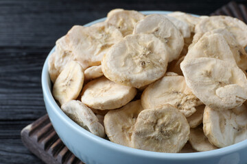 Bowl with dried banana slices on black wooden table, closeup