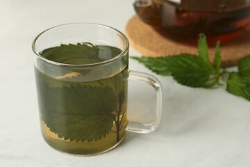 Glass cup of aromatic nettle tea on white table, space for text
