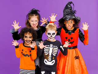 Happy Halloween! Kids in carnival costumes and makeup make a terrible gesture on bright colored purple background