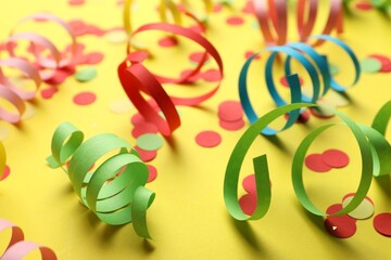 Colorful serpentine streamers and confetti on yellow background