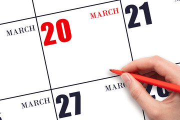 A hand holding a red pen and pointing on the calendar date March 20. Red calendar date, copy space,...
