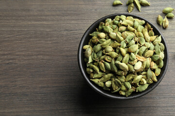 Bowl of dry cardamom pods on wooden table, top view. Space for text