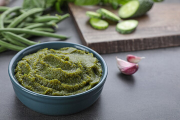 Bowl with tasty green puree and ingredients on black table, closeup