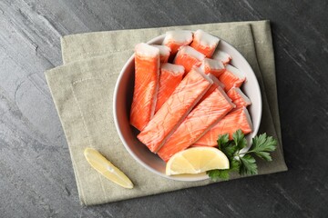 Crab sticks with lemon in bowl on grey table, flat lay