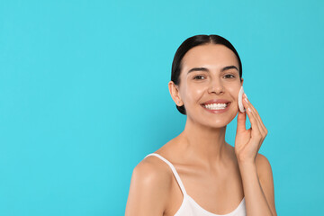 Young woman using cotton pad with micellar water on light blue background, space for text