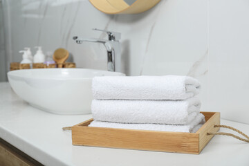 Wooden tray with rolled bath towels on white table in bathroom