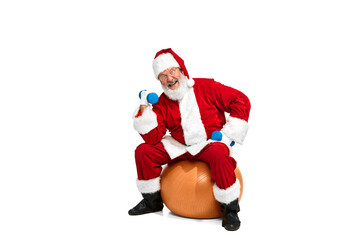 Portrait of senior man in image of Santa Claus on exercise ball and doing exercises with dumbbells over white background