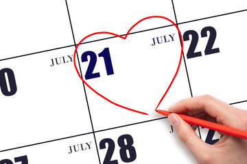 A woman's hand drawing a red heart shape on the calendar date of 21 July. Heart as a symbol of love.