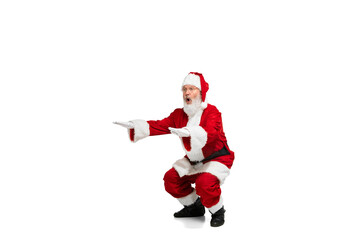 Portrait of senior man in image of Santa Claus training, doing squats isolated over white background