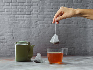 Hand picking up a tea bag, with a glass cup and green porcelain teapot