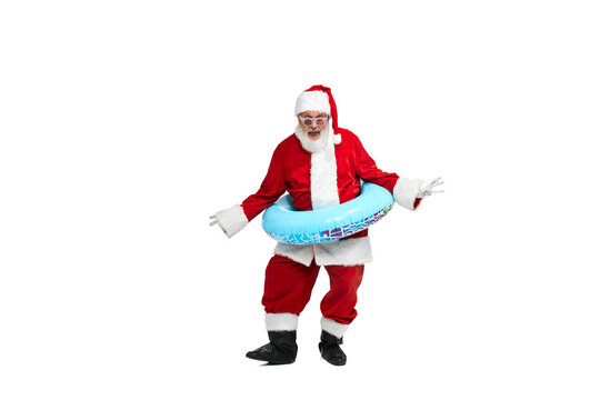 Portrait of senior man in image of Santa Claus posing with swimming circle and sunglasses isolated over white background.