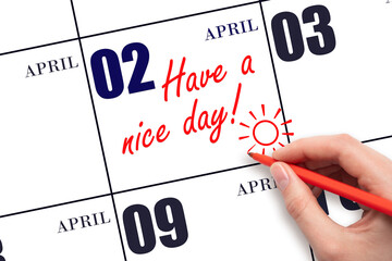 The hand writing the text Have a nice day and drawing the sun on the calendar date April 2