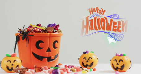 Image of halloween text over carved pumpkin bucket with sweets on grey background