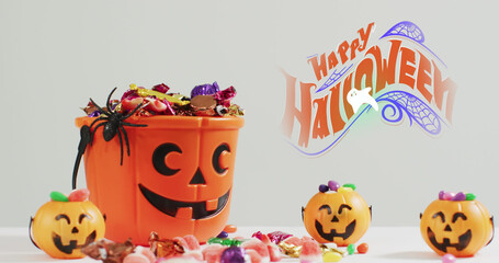 Obraz premium Image of halloween text over carved pumpkin bucket with sweets on grey background