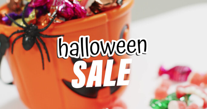 Image of halloween sale text over carved pumpkin bucket with sweets on grey background