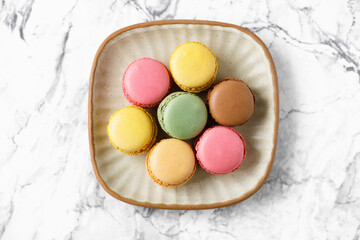 Various colorful macaroons on a plate on a marble table, top view