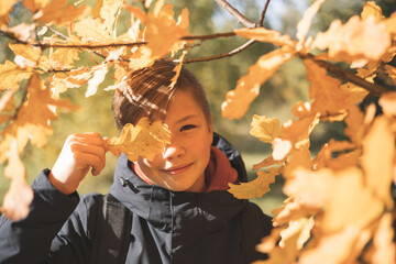 Autumn portrait of teenage boy with yellow oak leaf outdoors. Fall foliage. Smiling happy child walking in nature. Schoolboy having fun in autumn park.