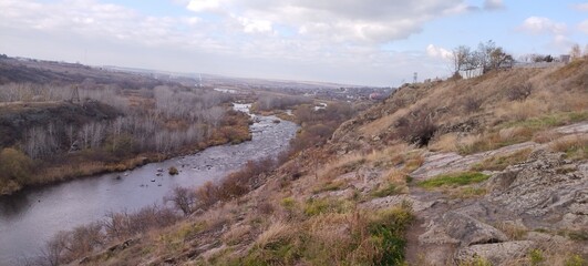 Rocky river bank among hills overgrown with vegetation, granite stones among dry yellowed grass