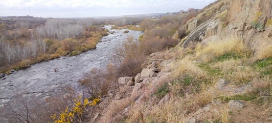 Rocky river bank among hills overgrown with vegetation, granite stones among dry yellowed grass