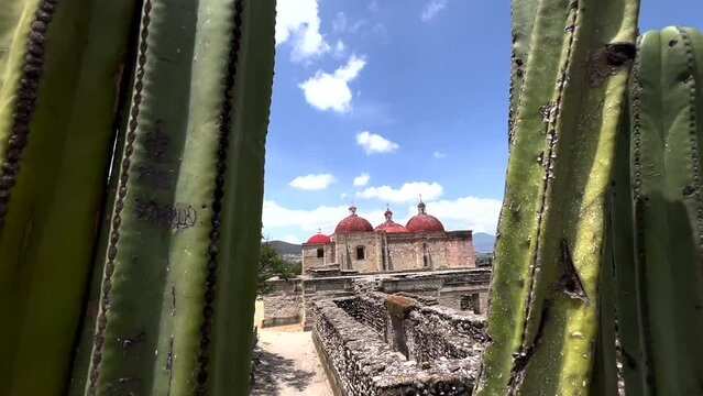 Ancient Ruins Site of Mitla Oaxaca Mexico, Dolly View Through Cactus Plant of Stone Ruins Walls, Architectural Church Religious Monument in Background, Famous Archeological and Cultural Touristic Site