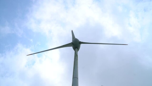 Windturbine Tower And Rotating Blades Against The White Clouds In The Sky. - low angle