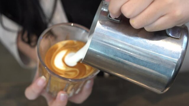 Professional skilful barista pouring frothed foamy milk into a cup of house blend espresso, making a beautiful latte art in the morning for the customer, food and beverages hospitality industry.