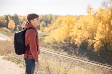 Teenager boy with backpack walking on path in autumn park. Active lifestyle, Back to school. Student boy in fall forest.