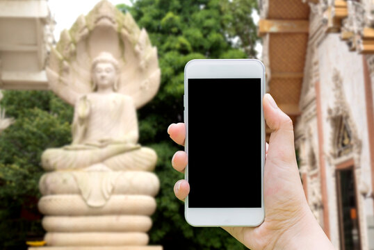 Hand Holding Mockup White Mobile Phone To Taking A Photo The Stone Statue Buddha With Blank Black Screen At The Temple In Thailand.