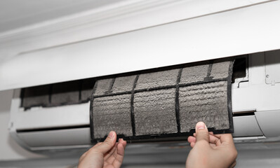 一只手正在取下积满灰尘的空调滤网