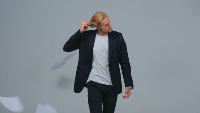 Young man in black suit, worker, architect, bank manager, student, reading notes then throwing them away, lets the hair down, takes off the jacket. Concept of freedom, end of the work day, fatigue.