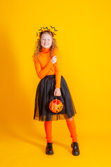 a teenage girl in a witch costume on a yellow background, holding a confent pumpkin eating marmalade worms halloween party