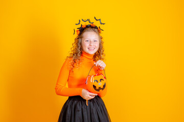 teenage girl in a witch costume on a yellow background, holding a confent pumpkin eating marmalade worms halloween party