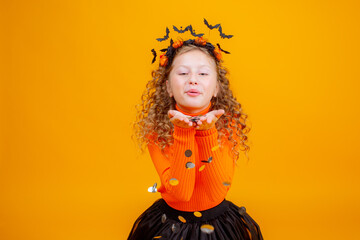 teenage girl in a witch costume on a yellow background, holding a confent pumpkin eating marmalade worms halloween party