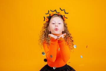 teenage girl in a witch costume on a yellow background, holding a confent pumpkin eating marmalade worms halloween party