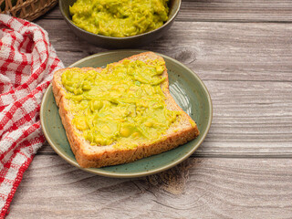 Top view of fresh guacamole on bread on a plate over a wooden table