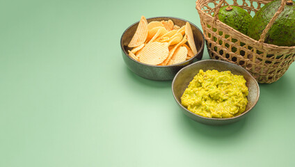 A bowl with fresh guacamole and potato chips on a plate over a green background