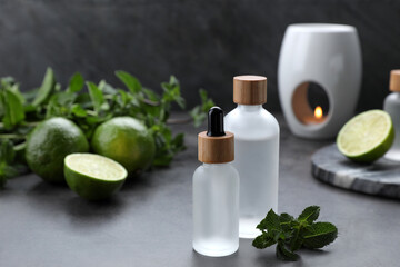 Bottles of essential oil, sliced limes and mint on grey table, space for text