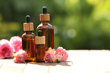 Fototapeta na wymiar Bottles of rose essential oil and flowers on wooden table outdoors, space for text