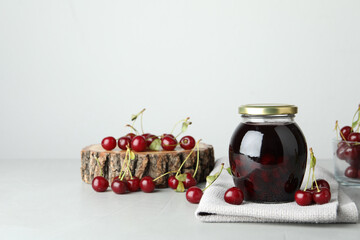 Fototapeta na wymiar Jar of pickled cherries and fresh fruits on light table. Space for text