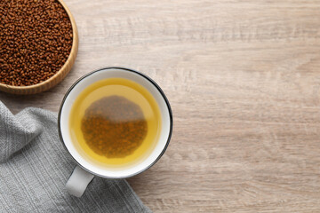 Buckwheat tea in cup and bowl with granules on wooden table, flat lay. Space for text