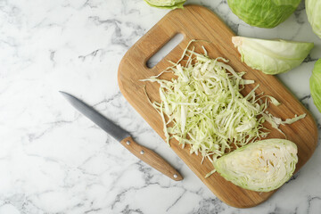 Chopped ripe cabbage and knife on white marble table, flat lay