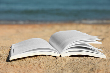 Open book on sandy beach near sea