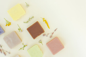 Handmade vegan soap made with natural herbal ingredients, herbs and flowers over light yellow background with copy space. Making skincare products at home. Flat lay style