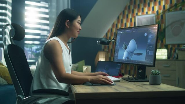 Asian woman creating 3D model of video game character in professional program using computer and digital tablet while working at home office