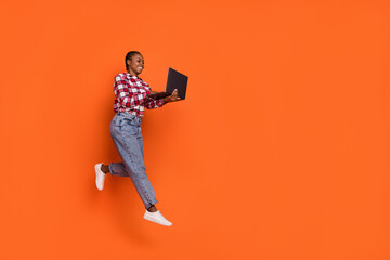 Full length photo of carefree excited person jump write email wireless netbook isolated on orange color background