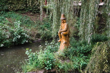a sitting wooden fairy tale character waterman in the middle of a pond surrounded by trees
