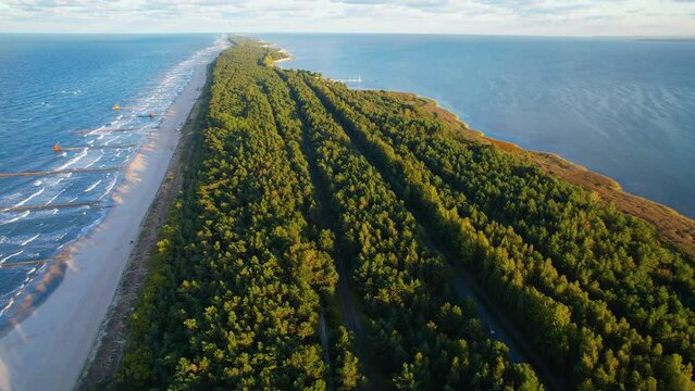 Aerial backwards flight over long green island of Zatoka Pucka during sunlight along sandy beach and blue Baltic Sea,Poland