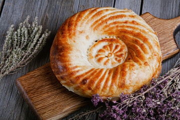 Uzbek tandyr flatbread. Traditional bread in Central Asia - tandyr flatbreadon (tandoor tortilla) on a wooden board on the table and sprigs of thyme and oregano