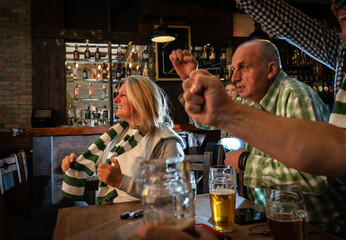 Mature football and soccer fans drinking beer at the pub and celebrating scores.