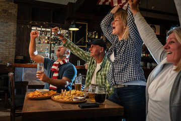 Mature football and soccer fans drinking beer at the pub and celebrating scores.